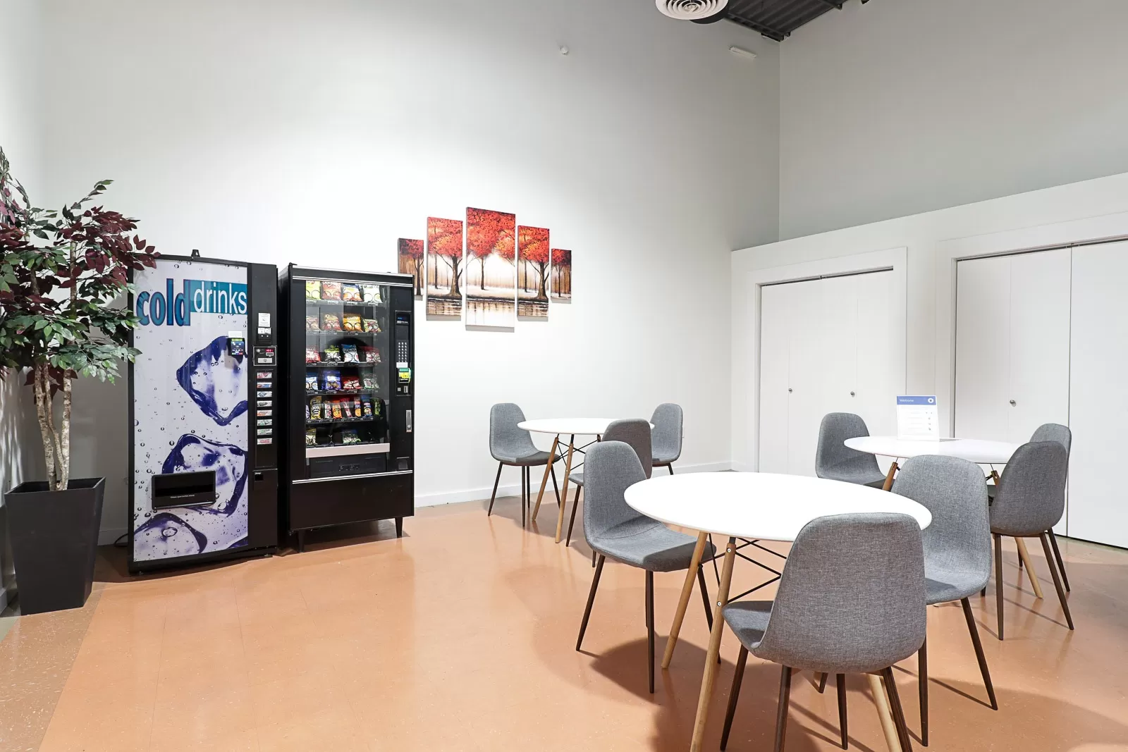 A room with chairs, tables and a vending machine.