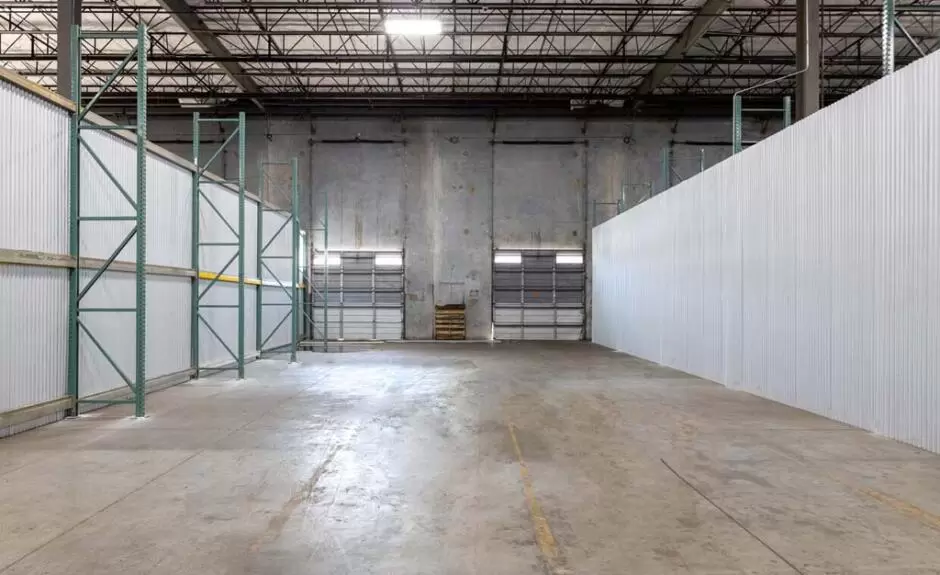 A large warehouse space with white walls, shelves, and 2 bay doors.