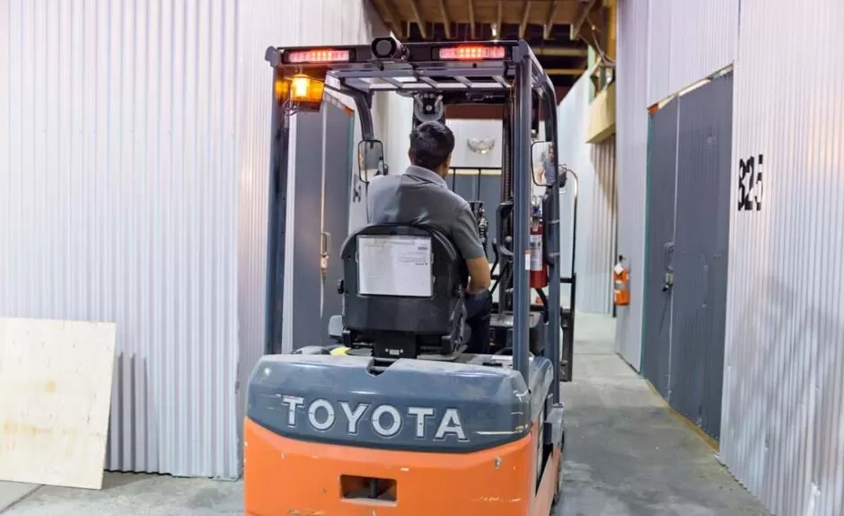 A man driving a toyota forklift in a warehouse.