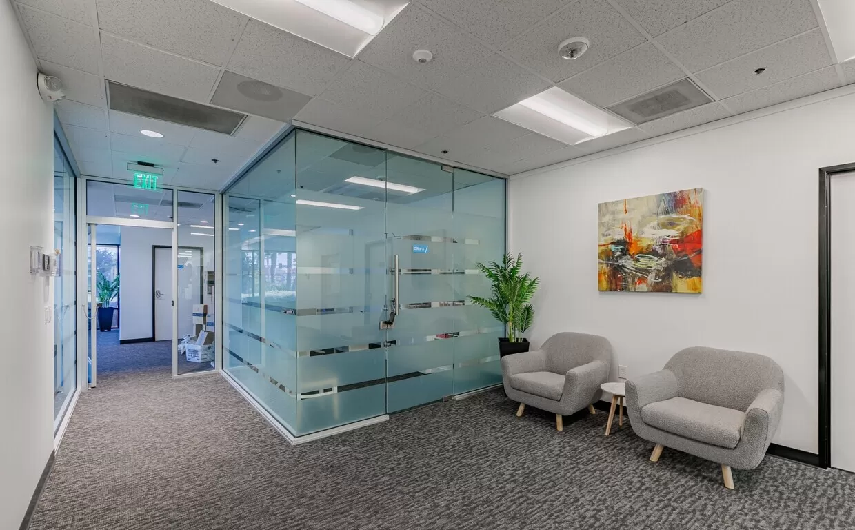 A glass walled office with chairs and a painting.